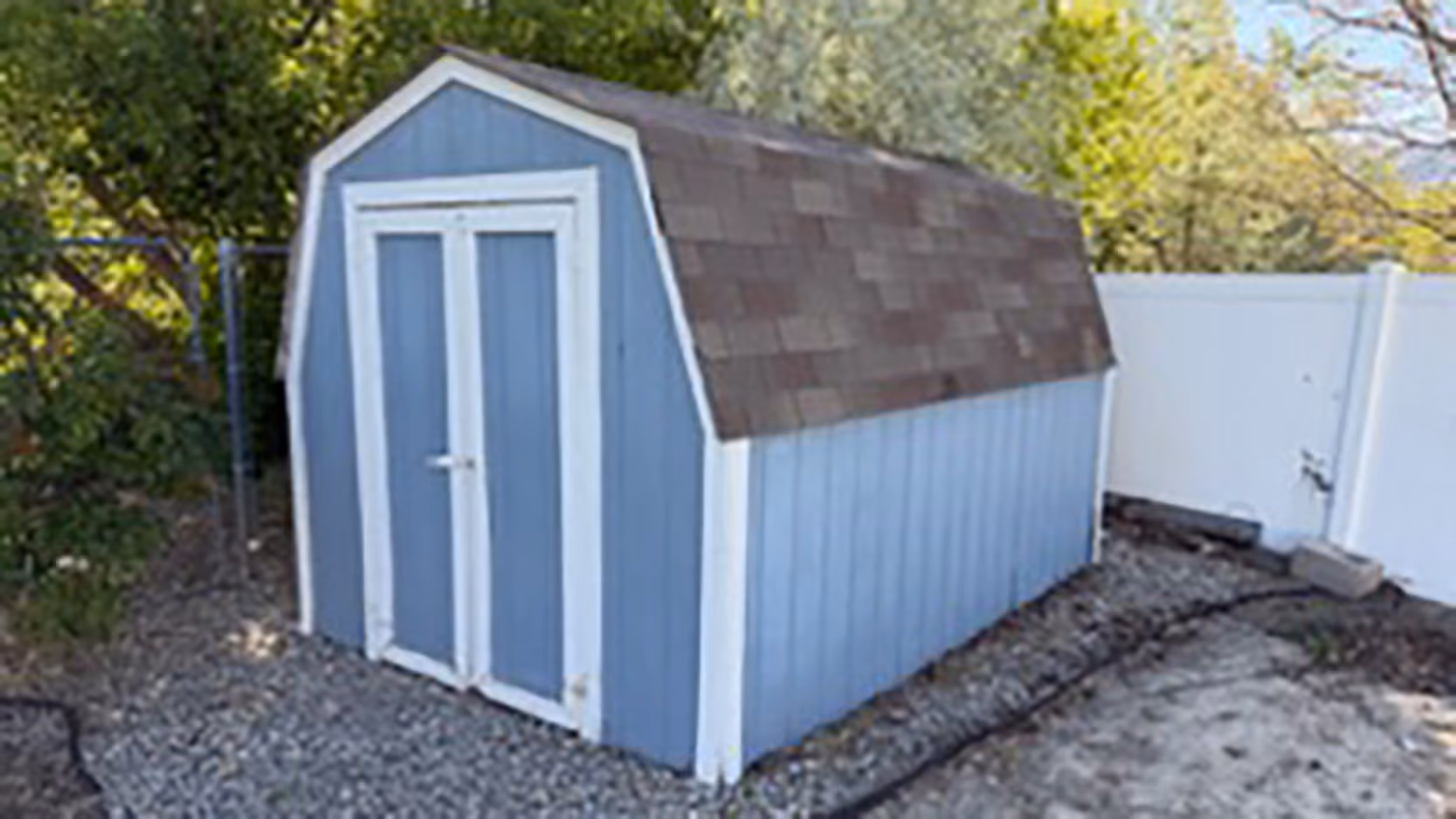 Angled view of a blue barn-style storage shed showing the front doors, side wall, roof, and surrounding access area.