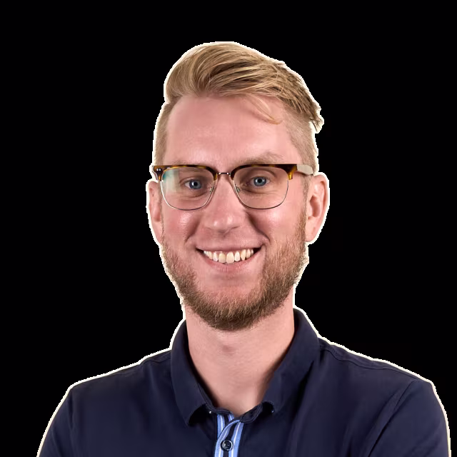 LJ Grab, smiling, with short blond hair, a beard, and thin-framed glasses, wearing a navy shirt