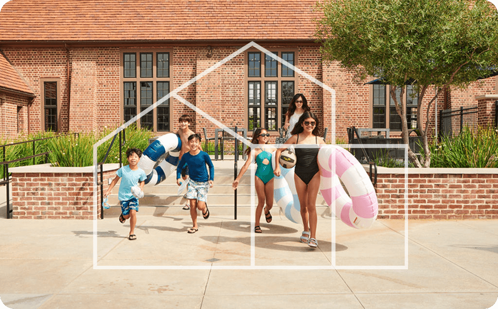ActionLife residents, including children with floaties, heading to the pool in front of a brick clubhouse.