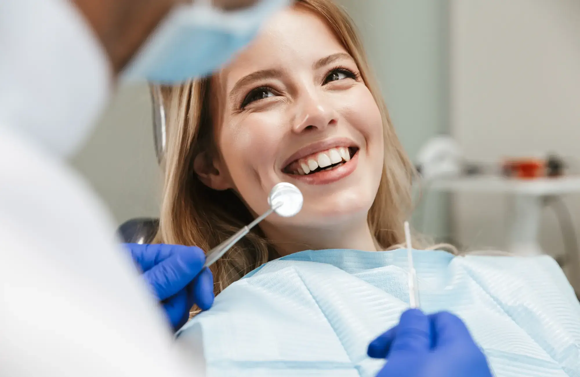 Woman smiling during a dental check-up while dentist holds a mirror and tool.