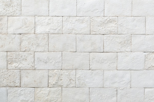 A close-up, straight-on shot of a wall made of light-colored, rectangular stone or tile blocks. The blocks vary slightly in size and texture, creating a rugged and natural-looking surface.