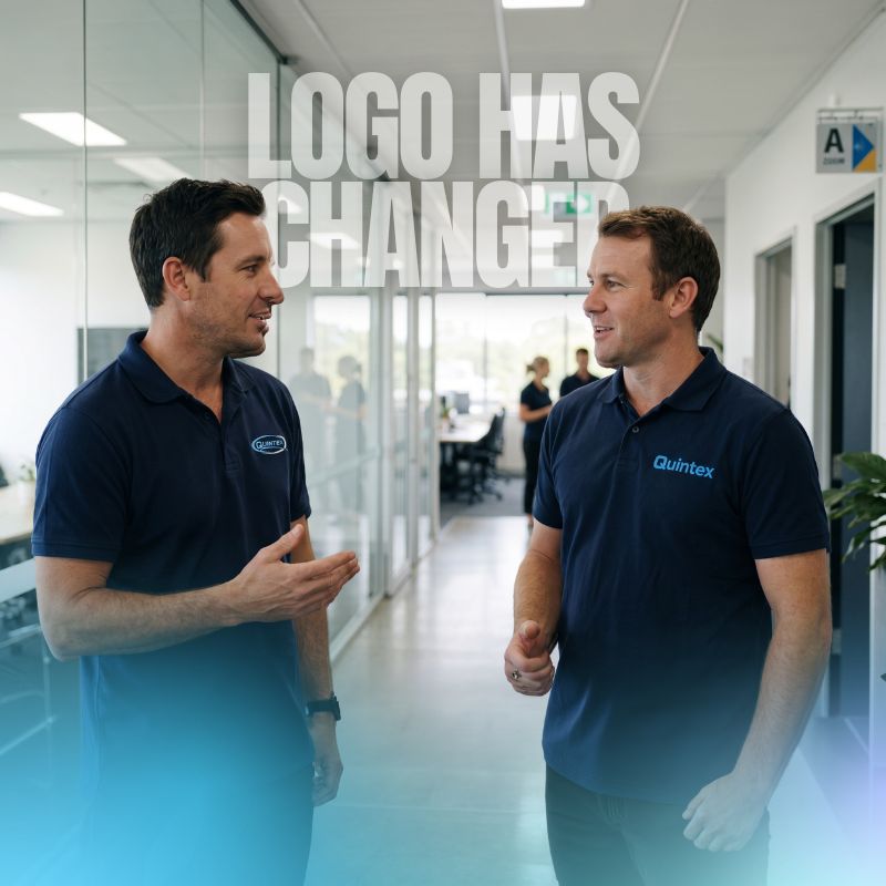 two employees standing in a hallway, speaking to each other. Logos on their polo shirts are visibly different.