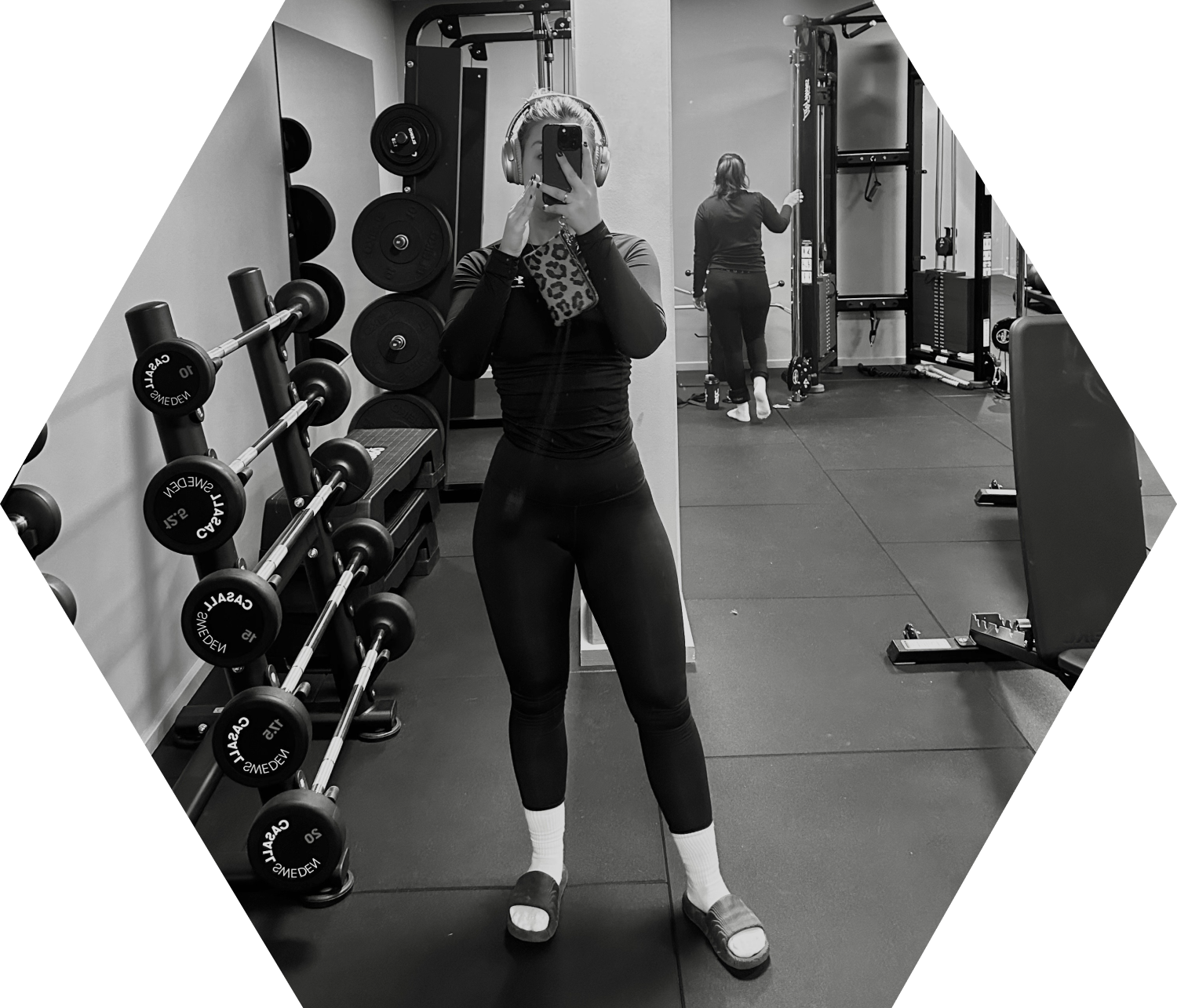 A focused woman in a gym holding a barbell towards her chest with both hands while looking straight ahead.