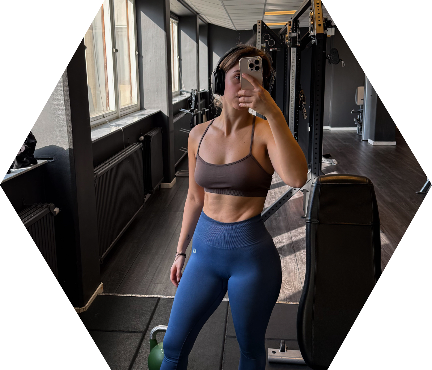 Photo of young fit woman in workout clothes, holding phone taking a mirror selfie