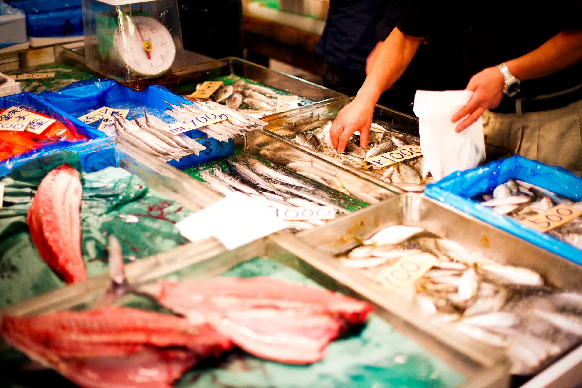 Asiatiskt urval av fisk och skaldjur med färsk marknadsdisplay med märkta priser och en försäljare som förbereder erbjudanden för försäljning.