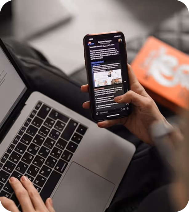 Person using a smartphone while working on a laptop.