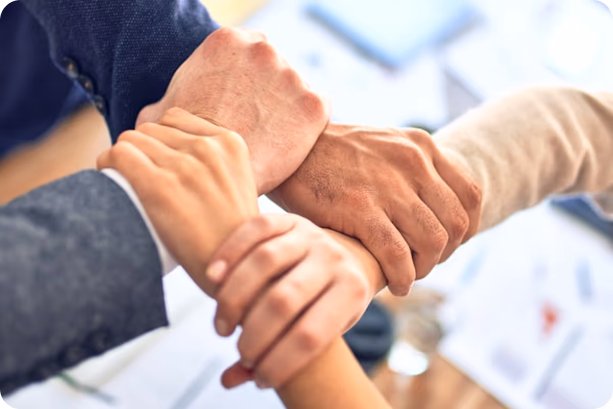 Close-up of four hands linked in a team-building gesture.