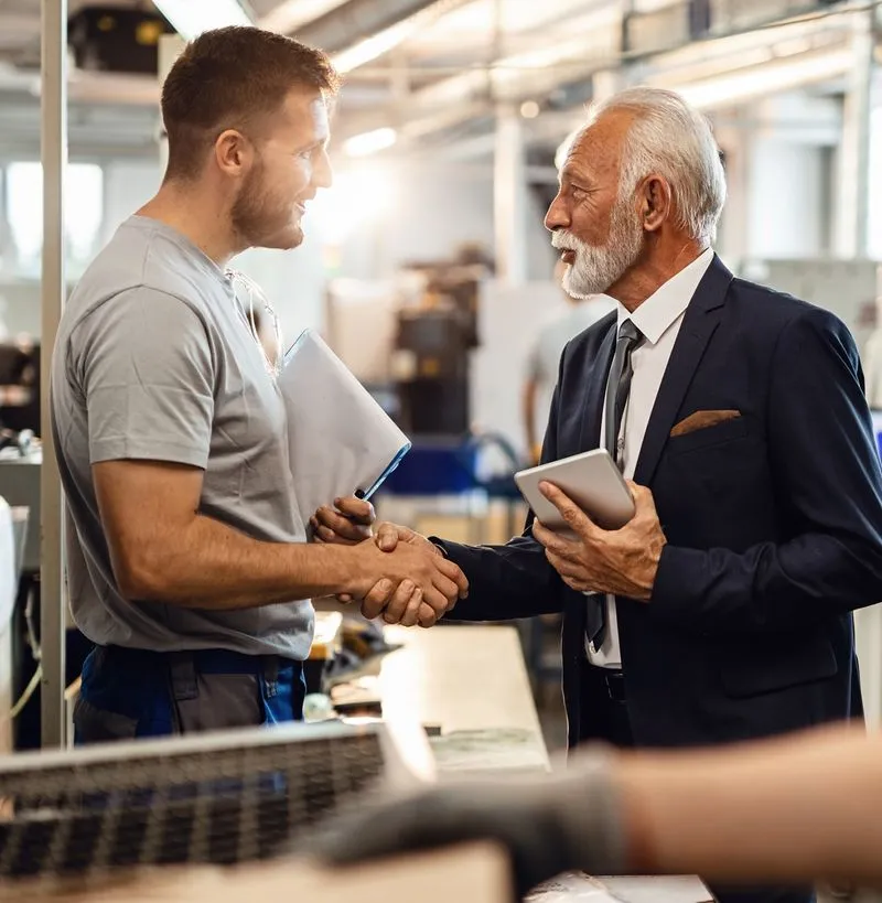 Man shaking another mans hand in a manufacturing setting