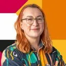 Person with orange hair and glasses wearing a colorful patterned jacket, smiling against a vibrant background.