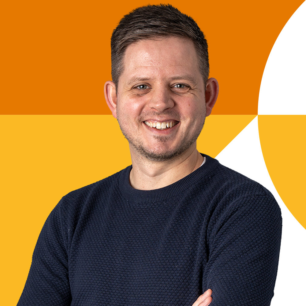 Smiling man with short hair in a dark blue sweater against an orange and yellow geometric background.
