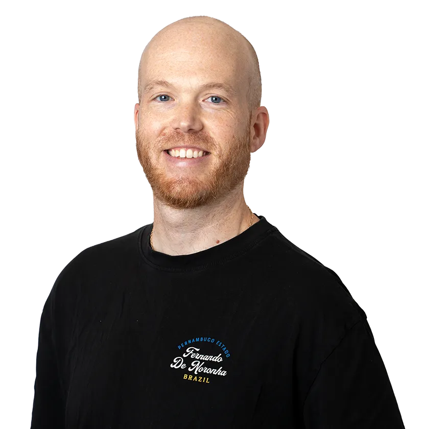 Smiling bald man with red beard wearing a black shirt with Fernando De Noronha Brazil text.