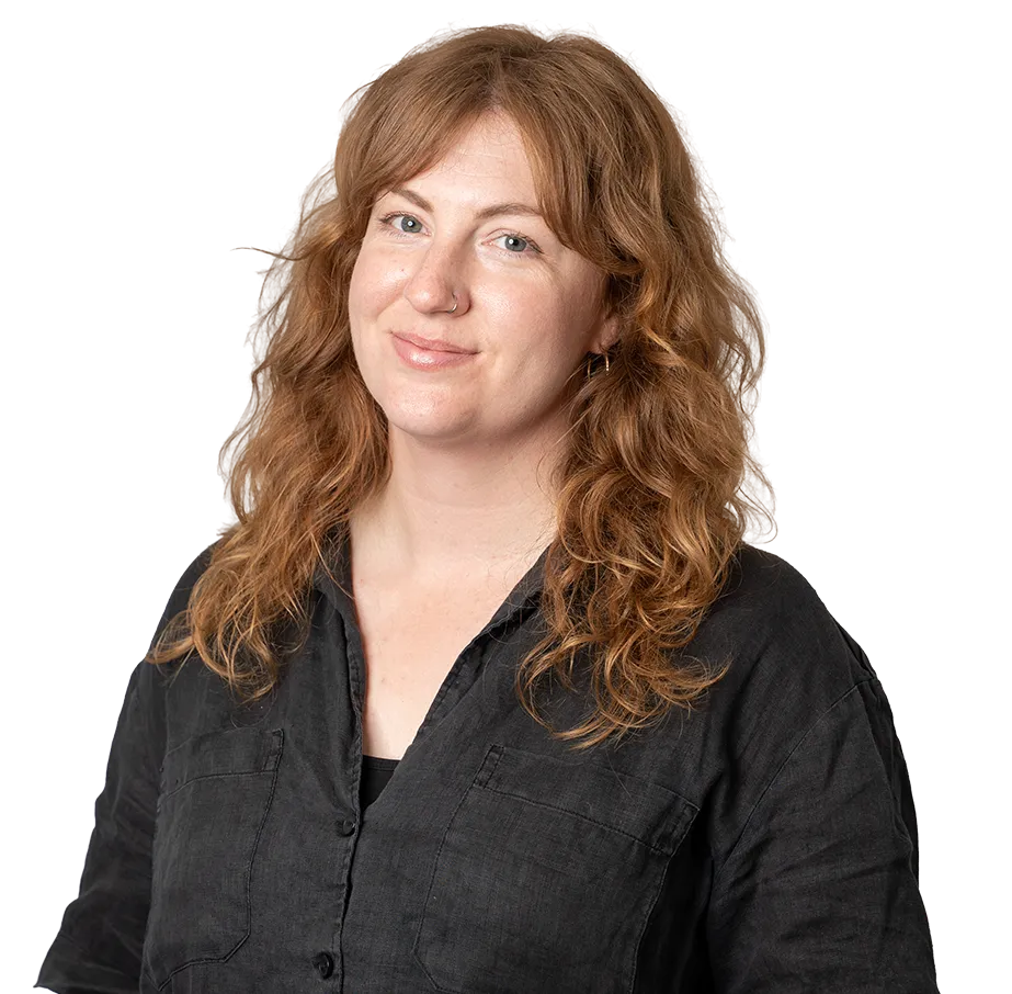 Smiling woman with curly red hair wearing a dark button-up shirt and small hoop earrings.