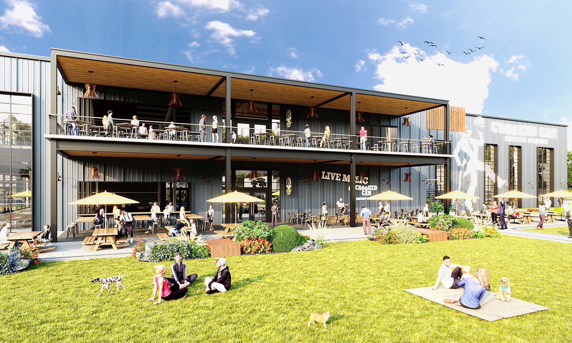 Outdoor dining area at a two-story modern restaurant with people sitting at tables and others relaxing on the lawn with dogs under a blue sky.