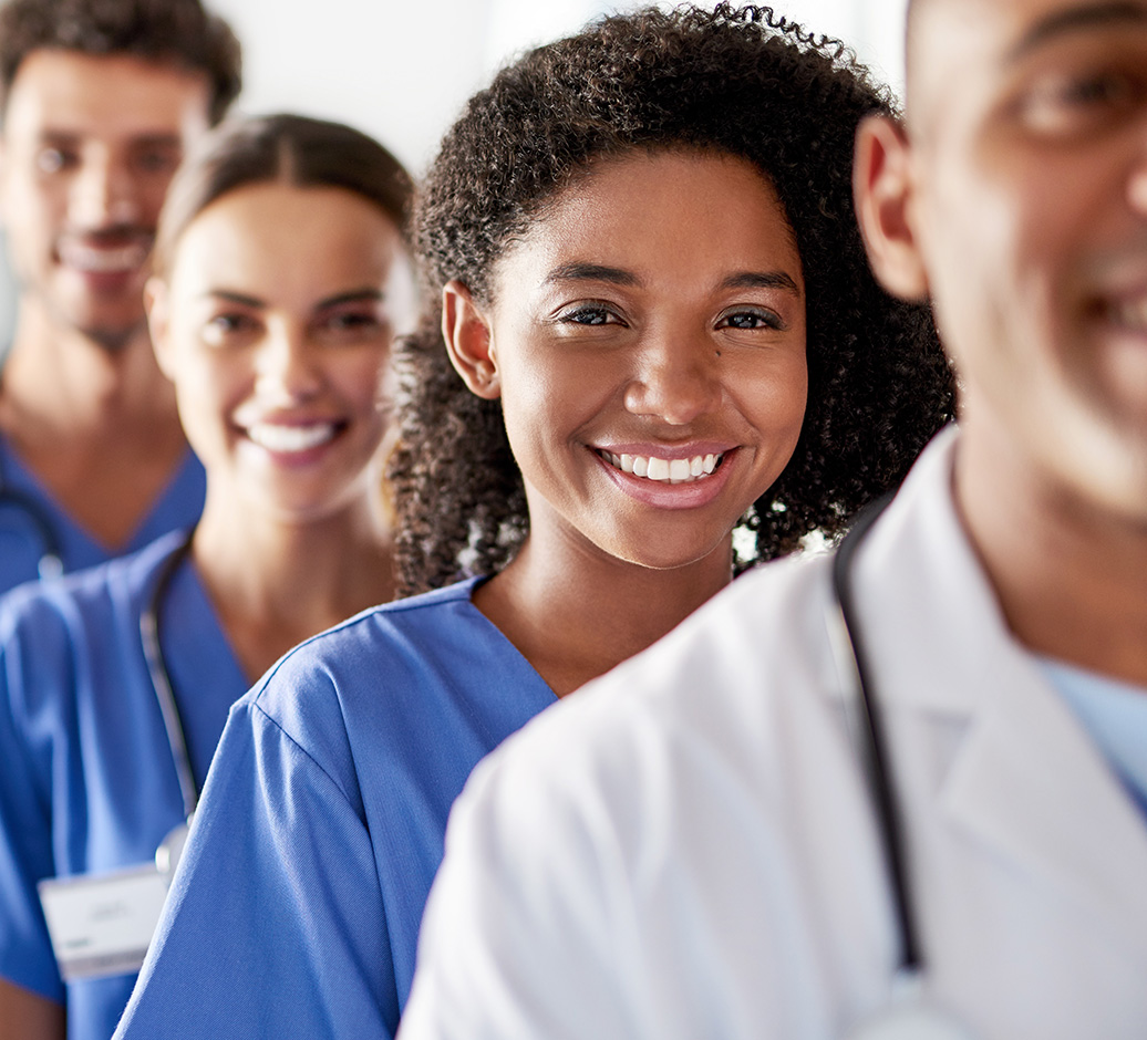 Smiling healthcare professionals in scrubs and lab coat standing in a line.
