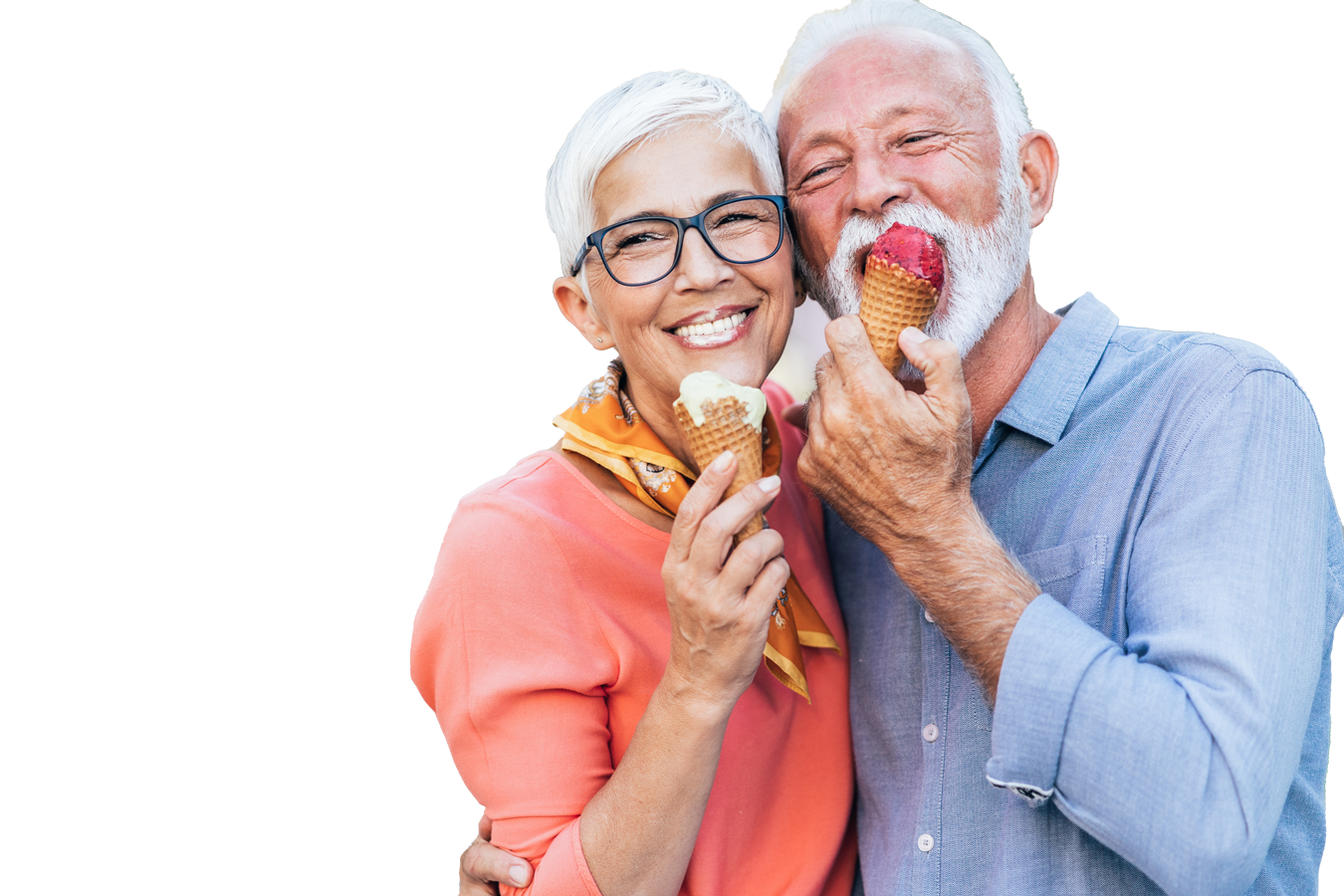 Smiling elderly couple enjoying ice cream cones outdoors, with the woman wearing glasses and a coral top and the man in a light blue shirt.