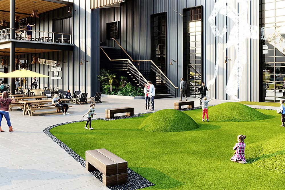 Children playing on artificial grassy mounds in an outdoor communal space with benches and modern building in the background.
