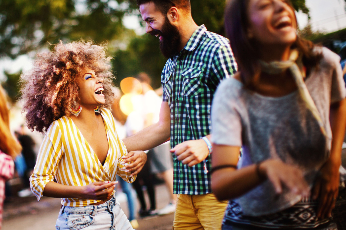 Three people laughing and enjoying an outdoor gathering with blurred background.