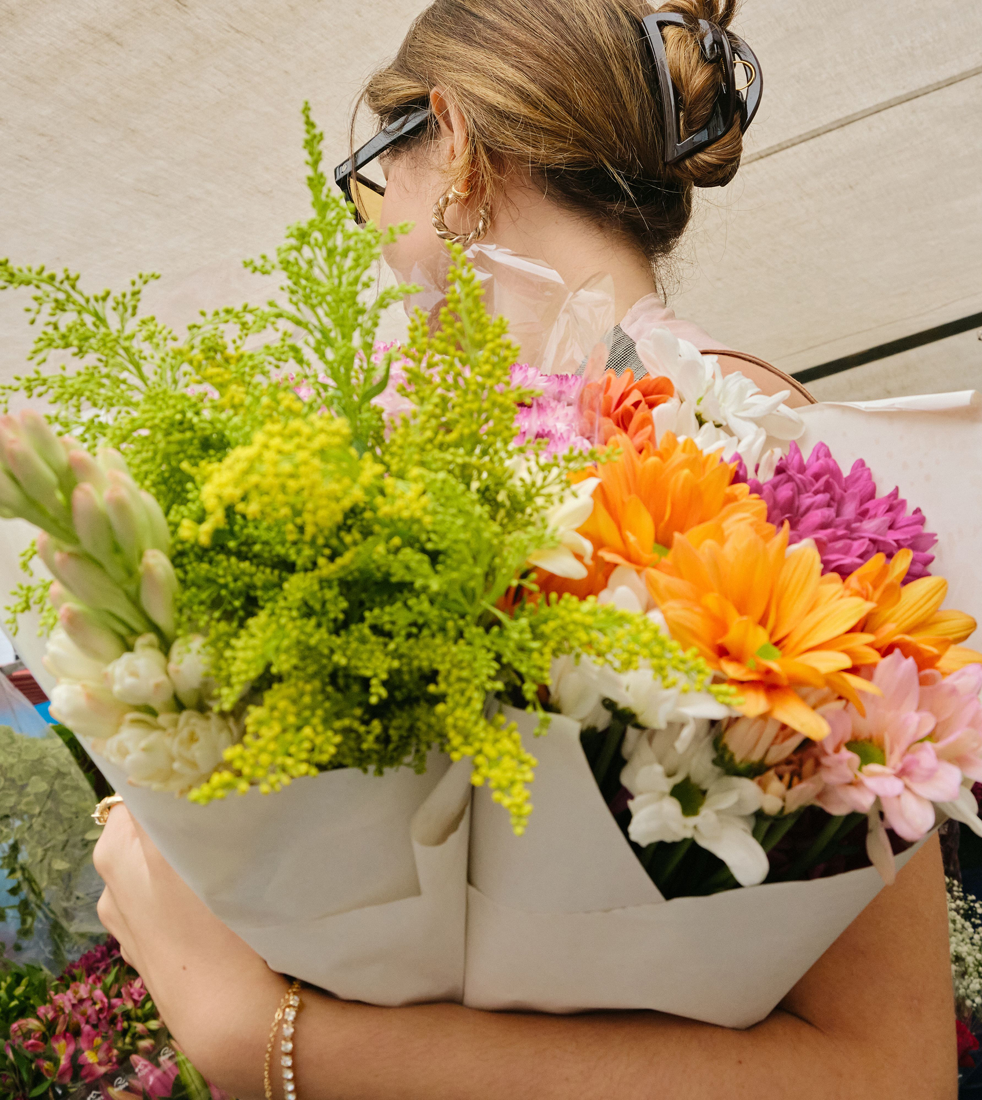 Person holding two large bouquets of assorted colorful flowers including orange, white, purple, and yellow blooms.