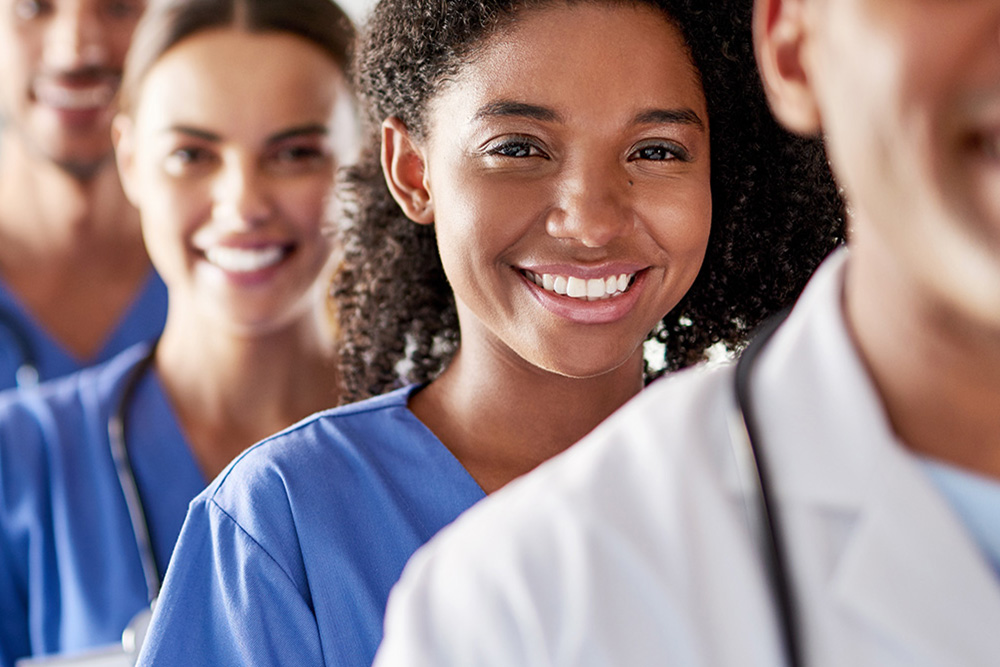 Smiling diverse healthcare professionals standing in a line wearing scrubs and lab coats.