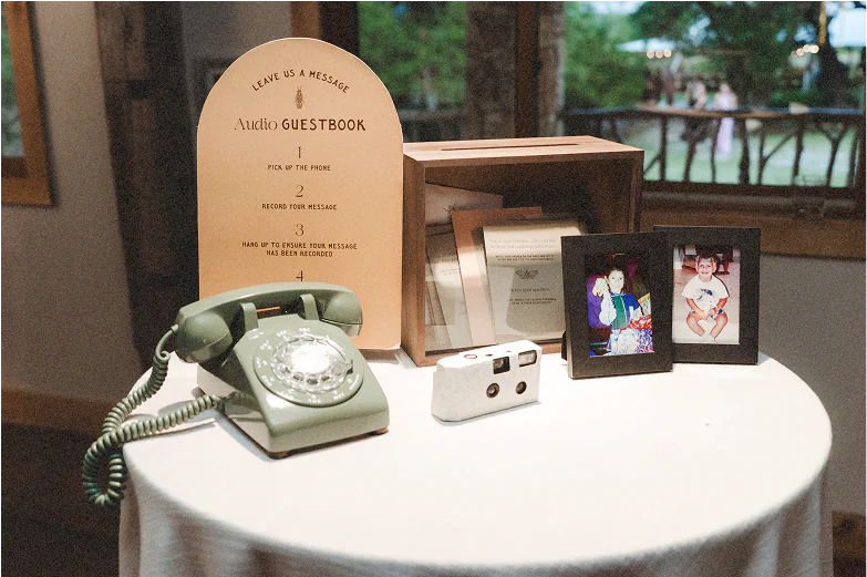 Vintage phone audio guest book on a table with a sign on how to use it, childhood photos, and a disposable camera.