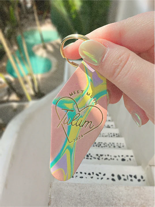 Hand holding a keychain with the phrase "Meet me in Tulum 2024" gold embossed on the front.