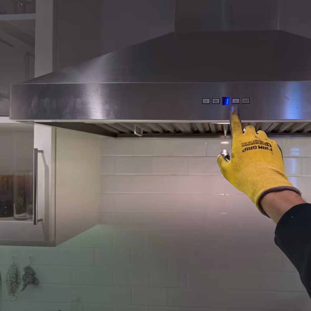 Yellow-gloved hand pressing button on stainless steel kitchen exhaust hood