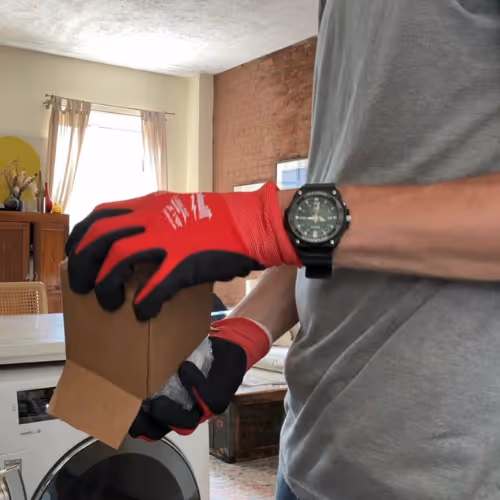 Person wearing red work gloves lifting cardboard box indoors