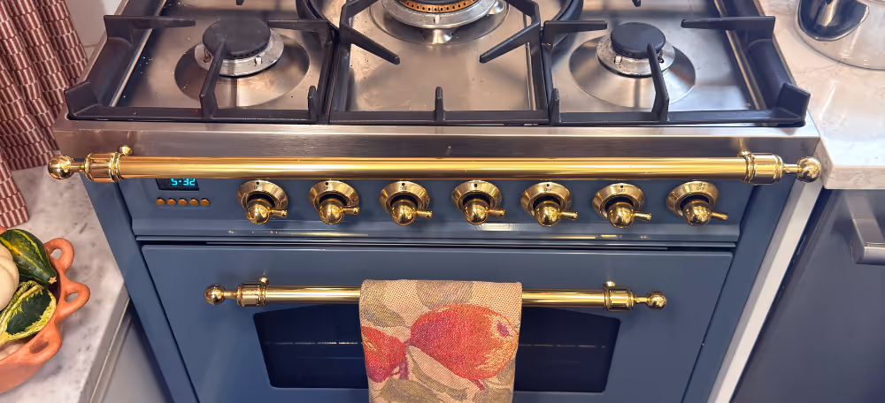 Blue gas stove with brass knobs and handles, a colorful towel hanging on the oven door, and a digital clock showing 5:32.