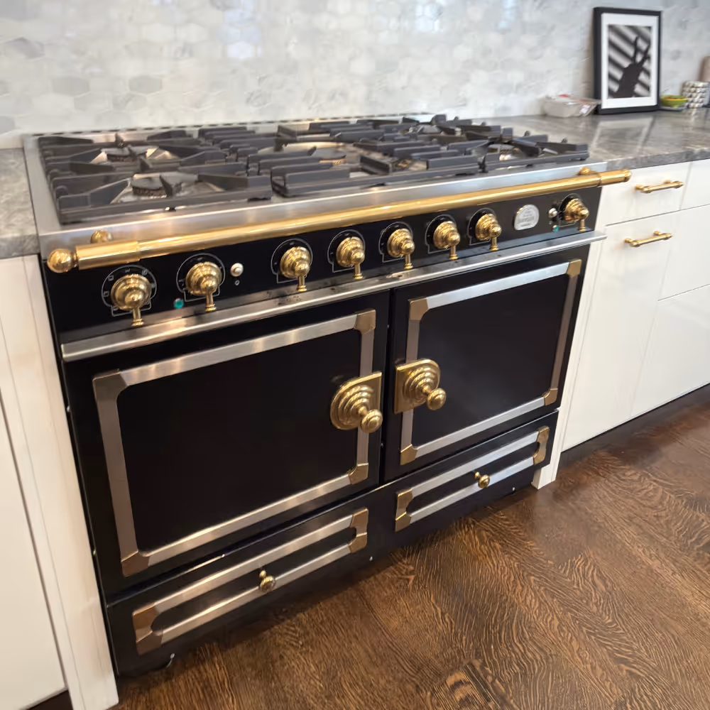 Black and gold double oven gas stove with multiple burners on top in a modern kitchen.