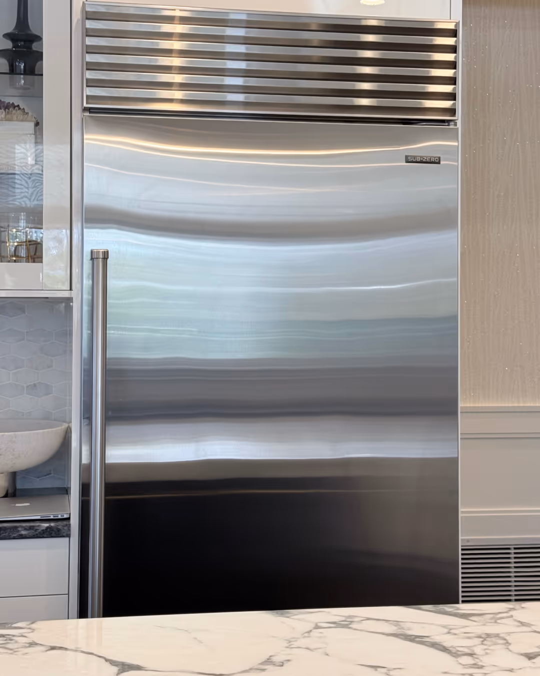 Stainless steel Sub-Zero refrigerator with a long handle in a modern kitchen setting.