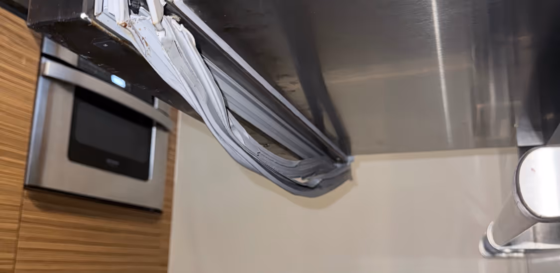 Close-up of damaged rubber seal on the door of a stainless steel refrigerator in a kitchen.