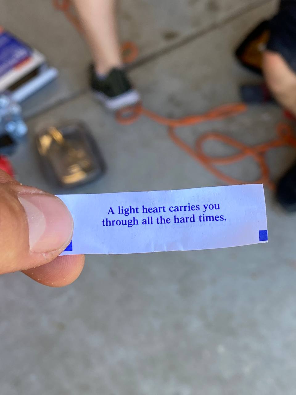 A hand holding a fortune cookie slip that reads, 'A light heart carries you through all the hard times.'