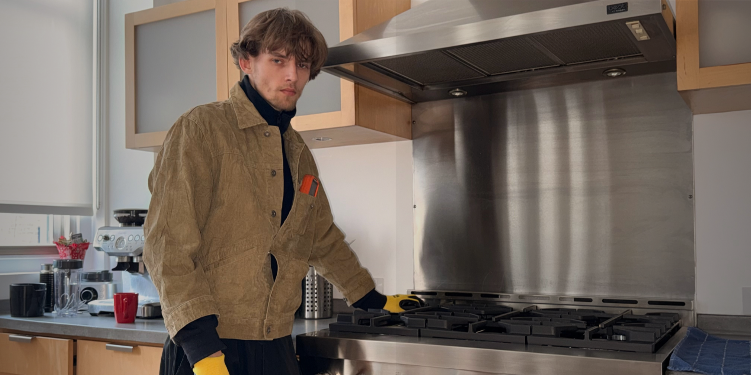 Modern kitchen corner featuring a stainless steel glass-door refrigerator, wooden cabinets, a mounted flat-screen TV, and a coffee machine on the countertop.