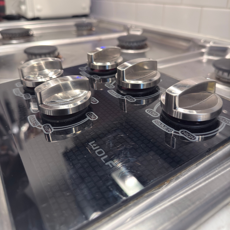 Close-up of a stainless steel Wolf gas cooktop with five control knobs and burner caps.