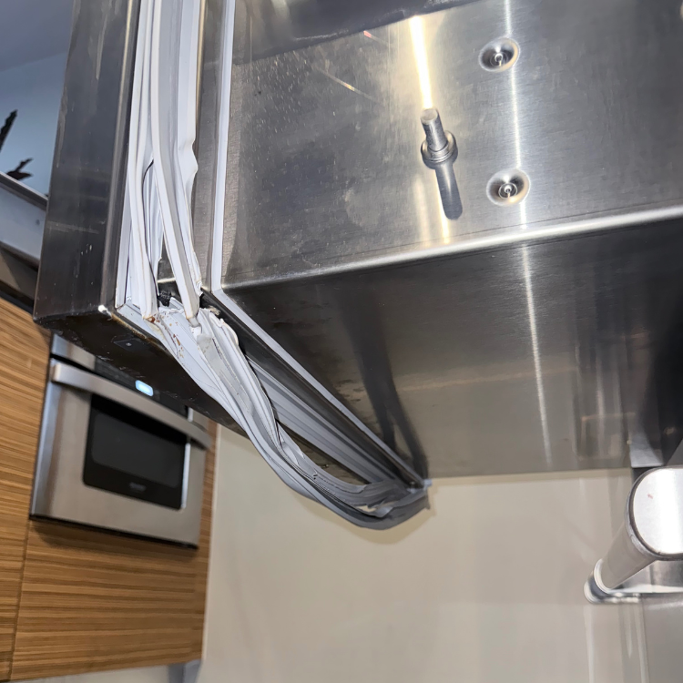 Close-up of a damaged and twisted white door gasket seal on a stainless steel appliance.