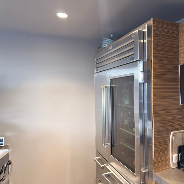 Modern stainless steel refrigerator with glass door in a kitchen featuring wood paneling and gray walls.