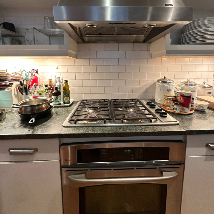 Modern kitchen stove with four gas burners, stainless steel oven below, and a countertop holding kitchen utensils, bottles, and jars.