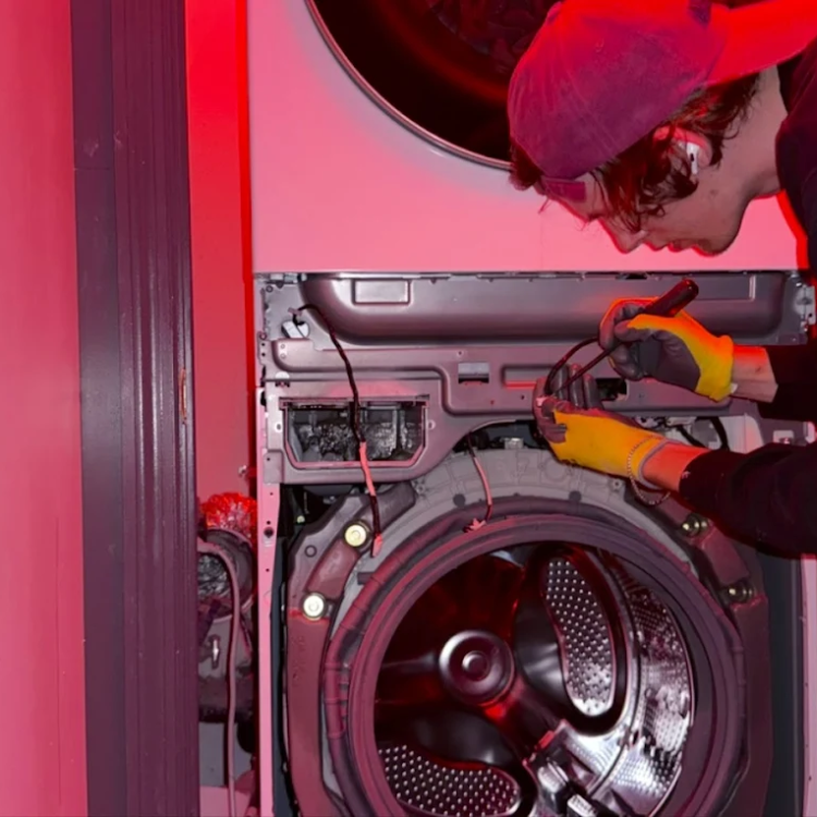 Technician with yellow gloves and red cap repairing the inner components of a front-loading washing machine.