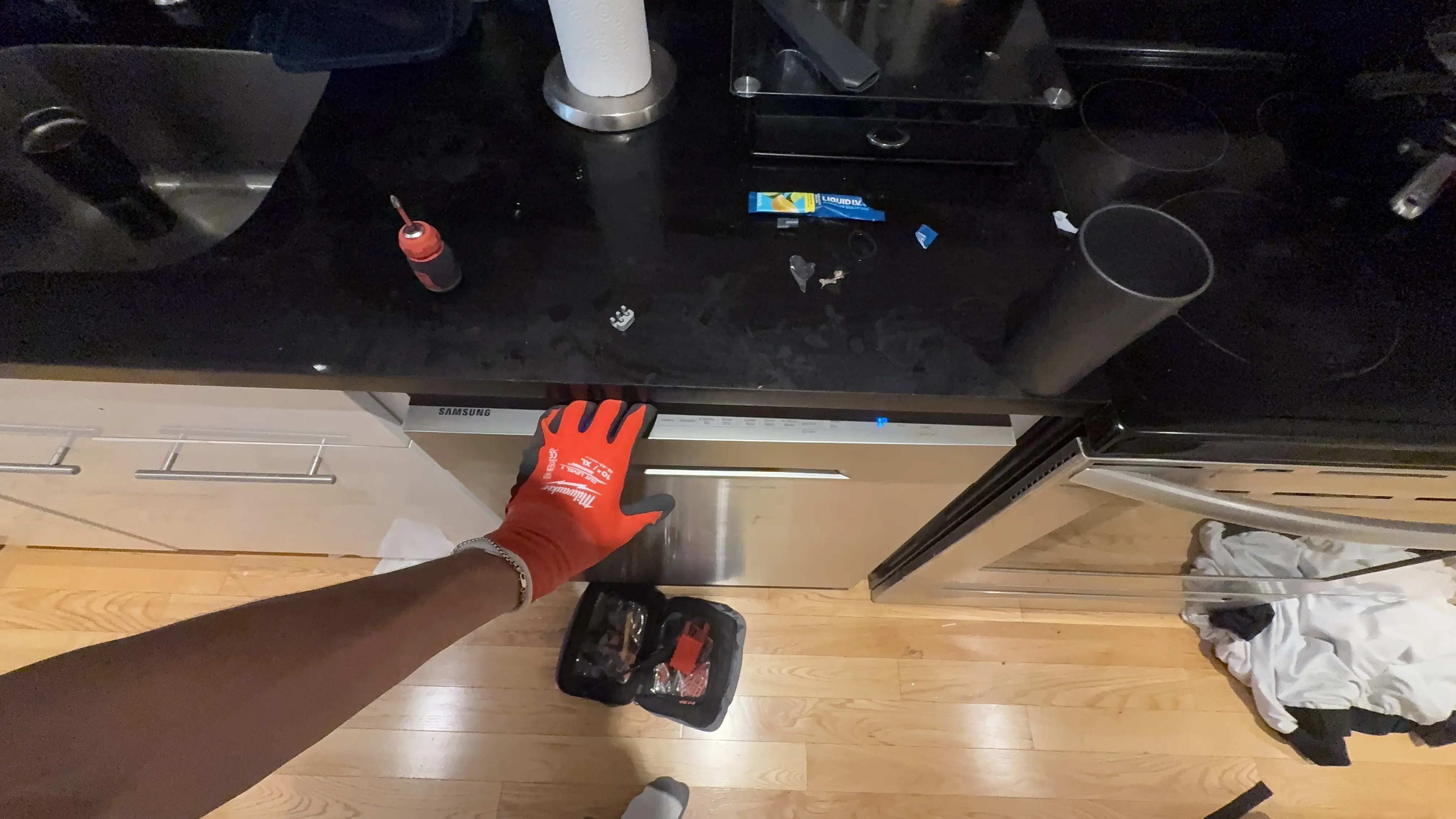 Hand in red work glove near kitchen drawer with tools and workspace