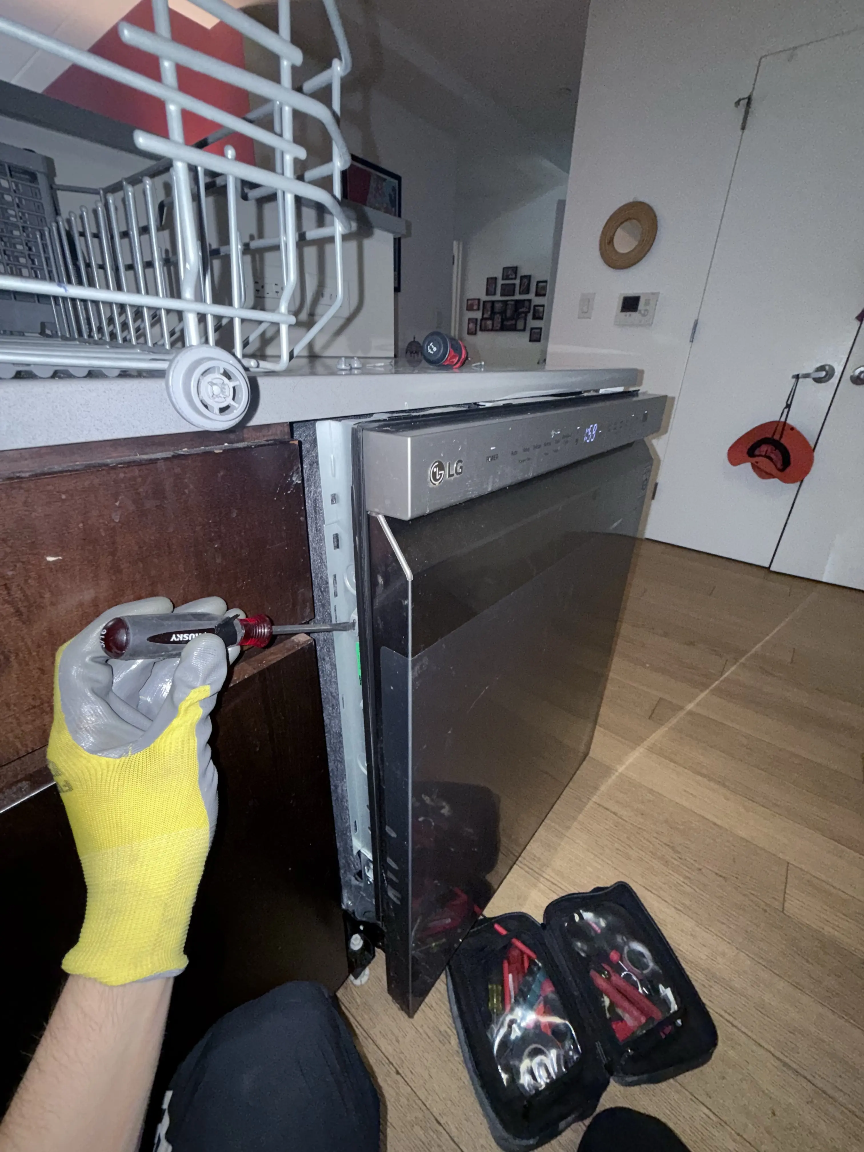 Technician repairing dishwasher with tools and yellow work glove