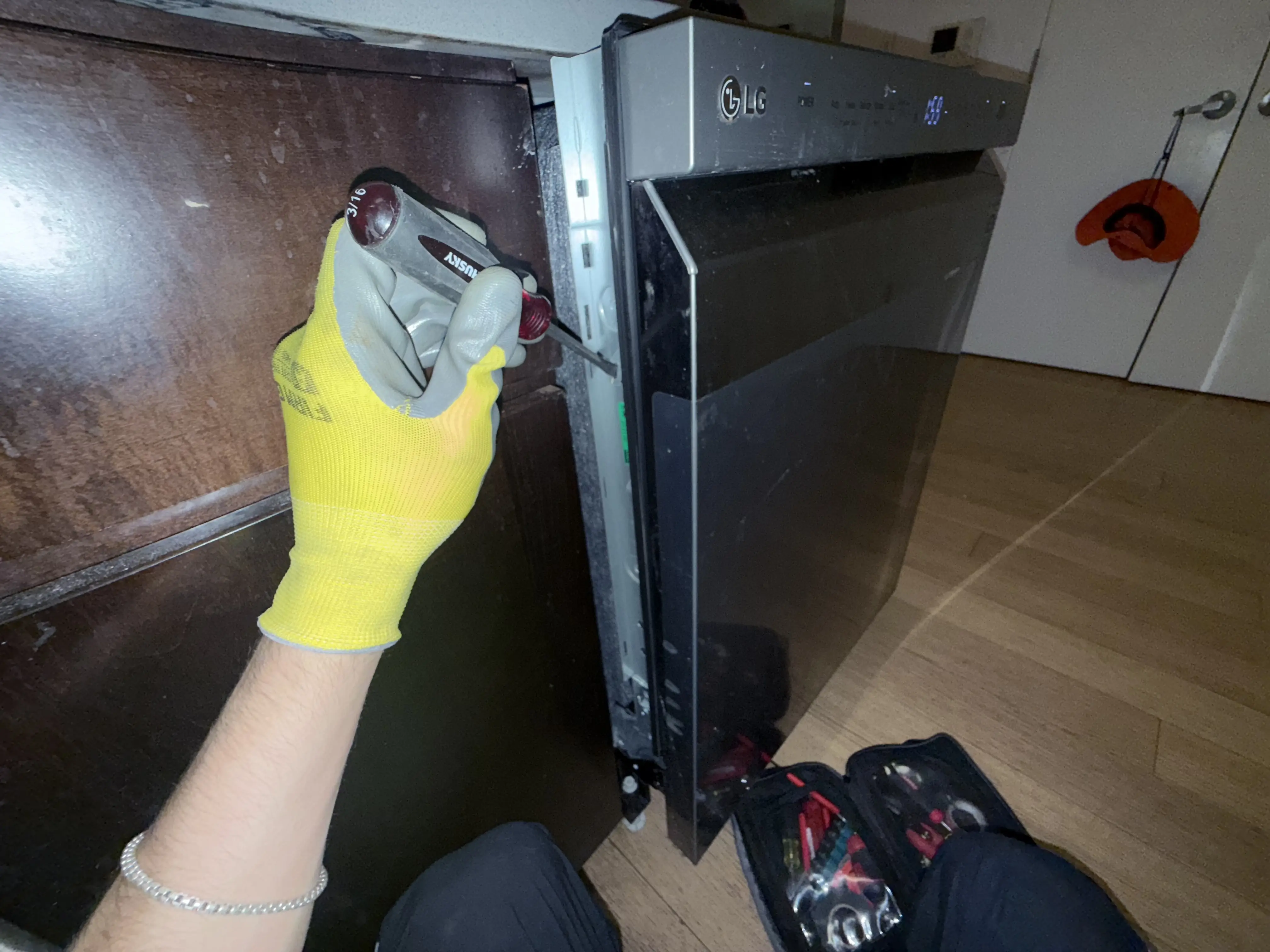 Hand in yellow glove using drill near LG appliance on wooden floor