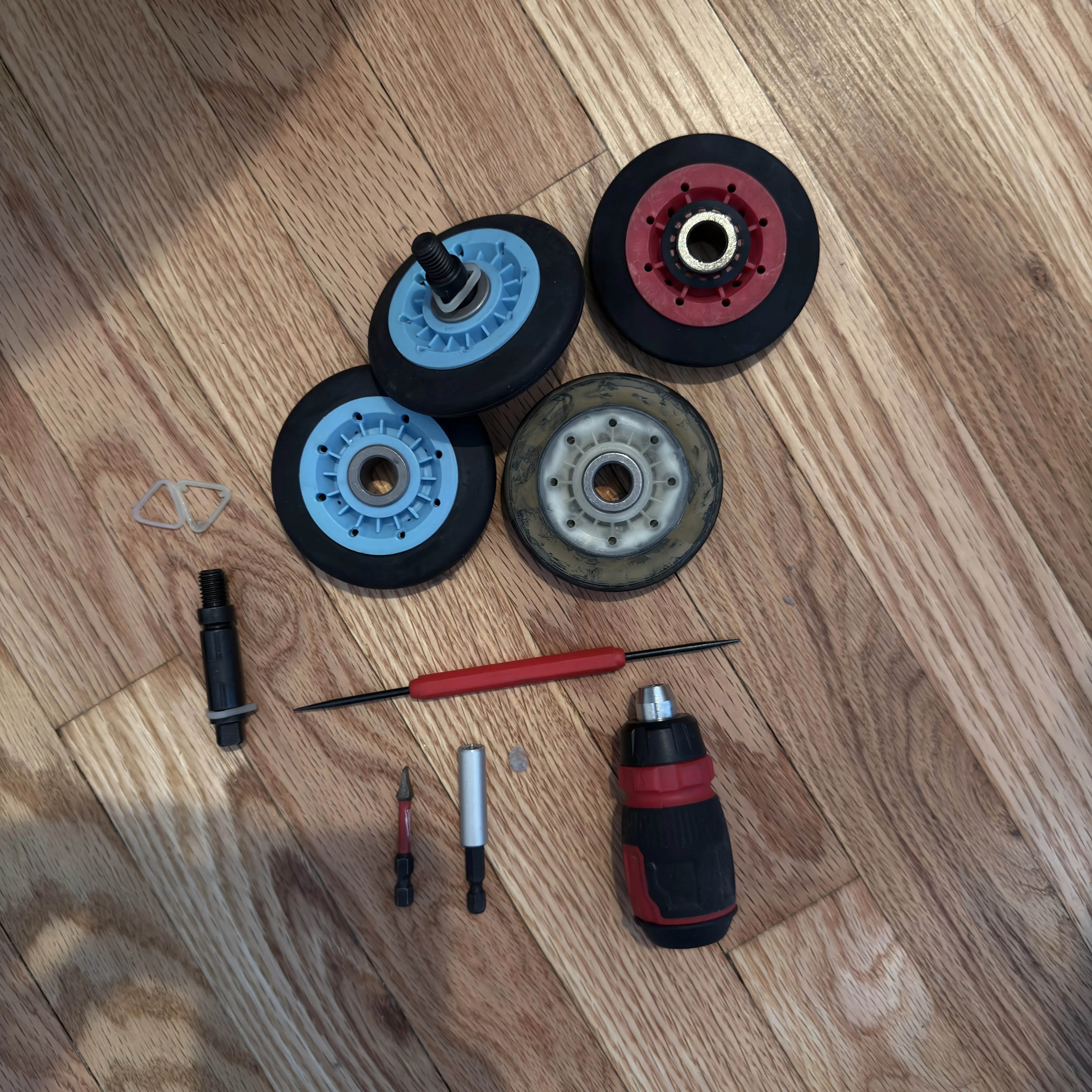 Disassembled dryer parts including rollers, shaft, and screwdriver on wood floor