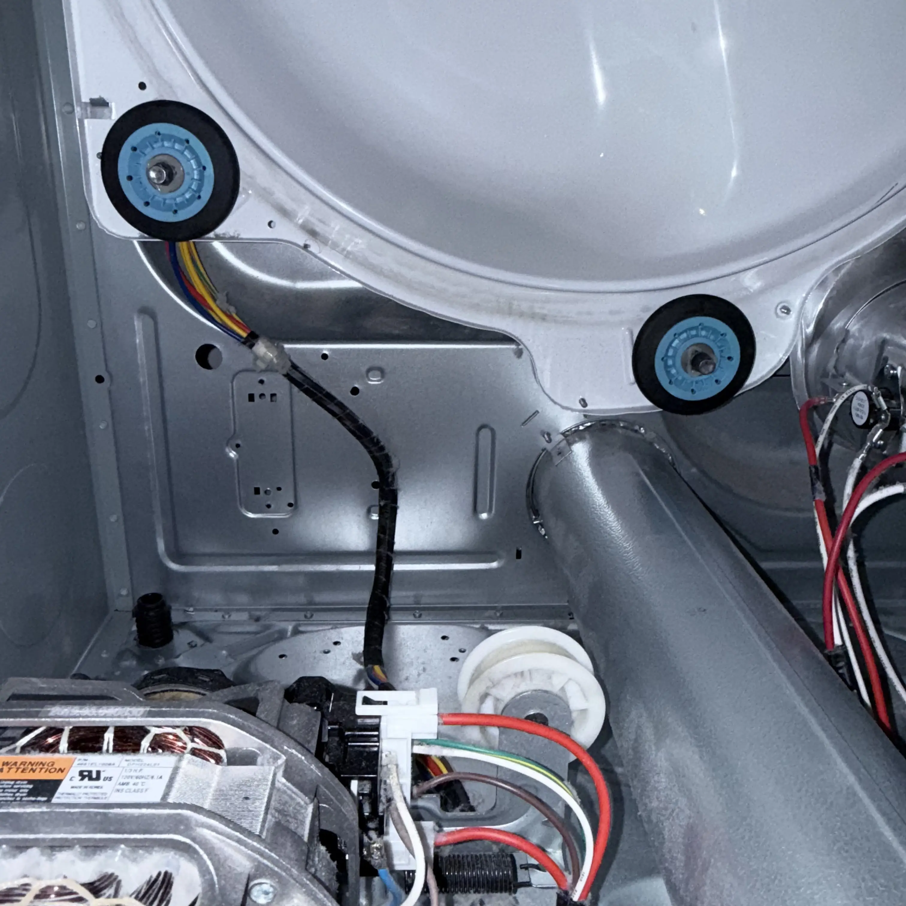 Inside of a dryer showing motor, wires, pulleys, and electrical components