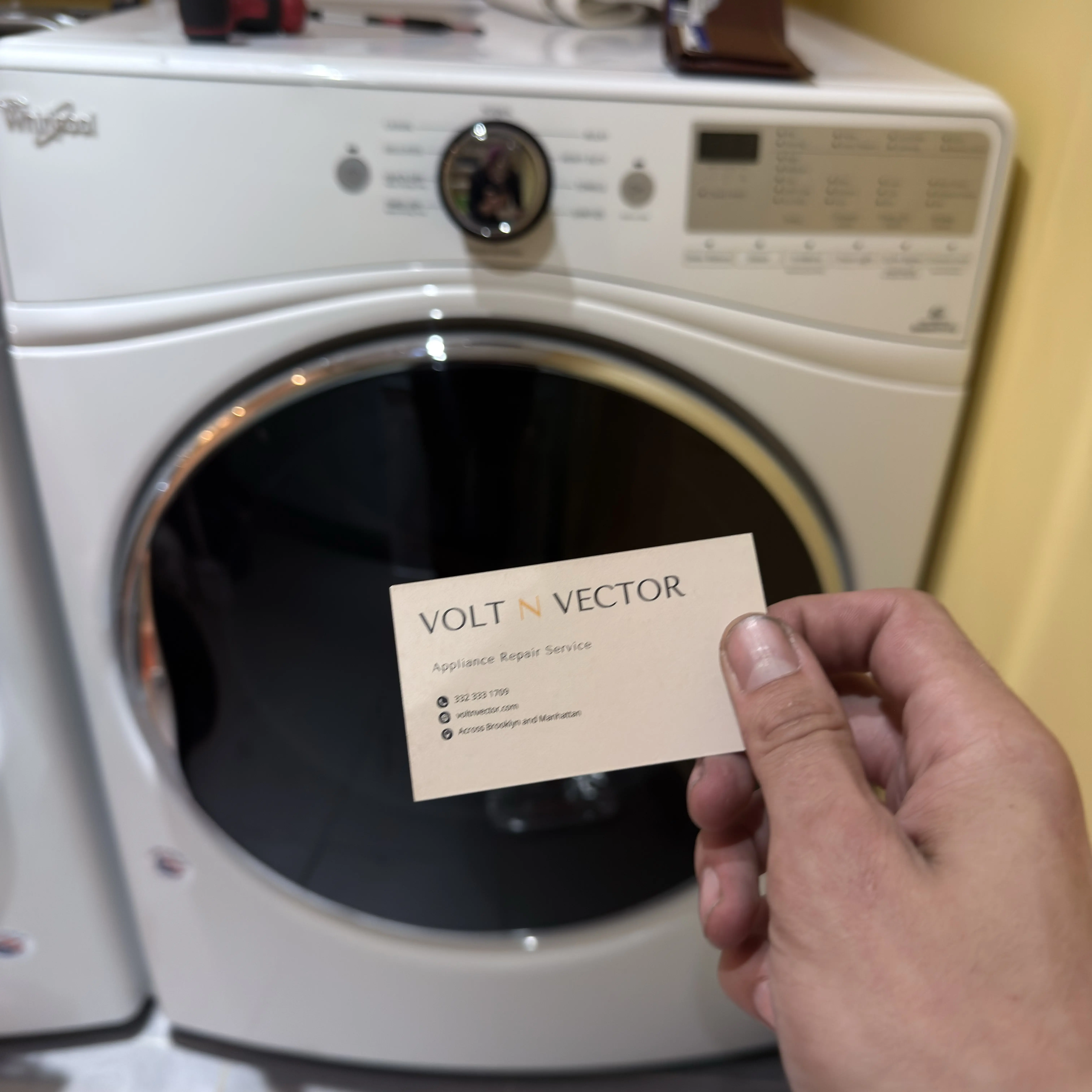 Hand holding Volt N Vector business card in front of a washing machine