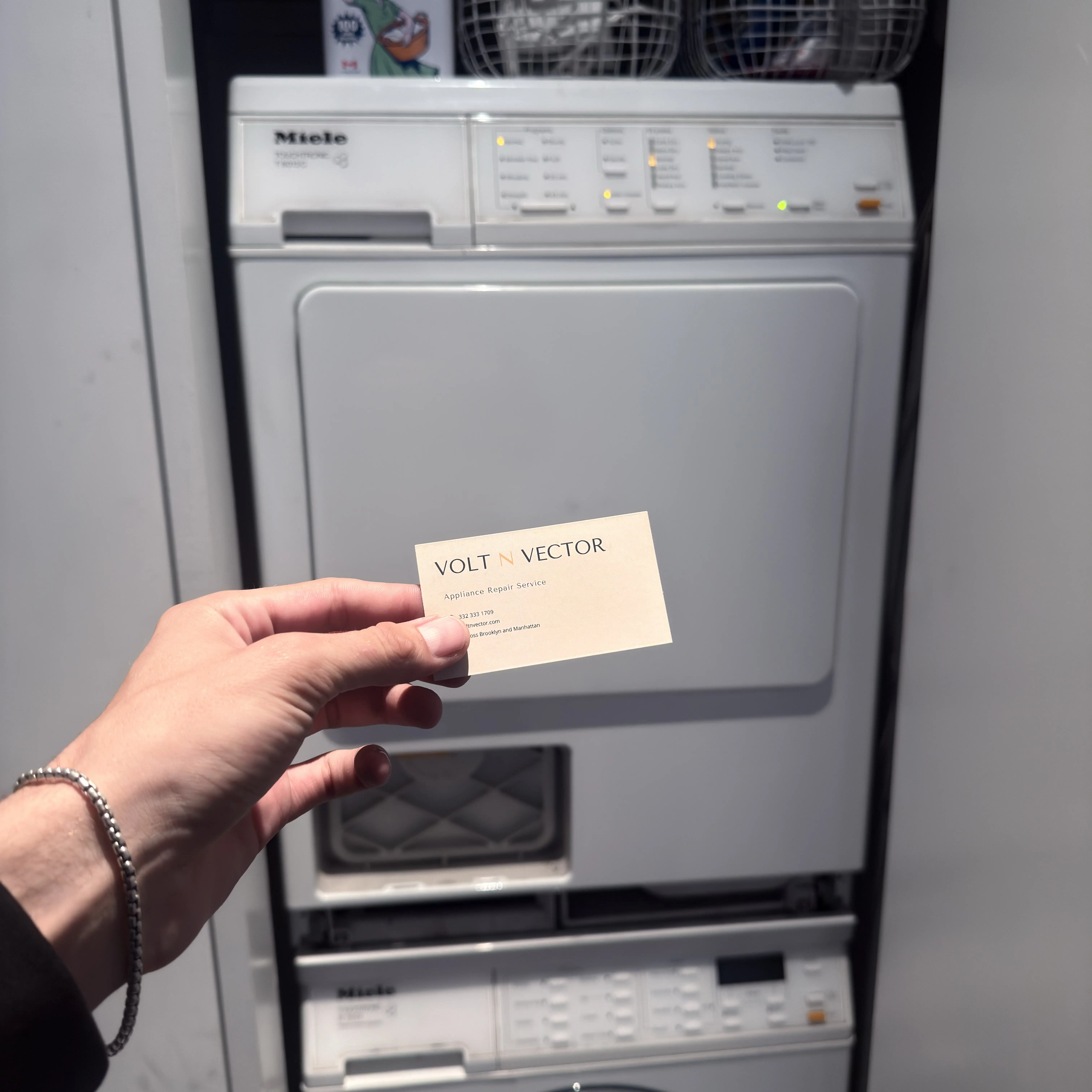 Hand holding Volt Vector business card in front of Miele washer and dryer