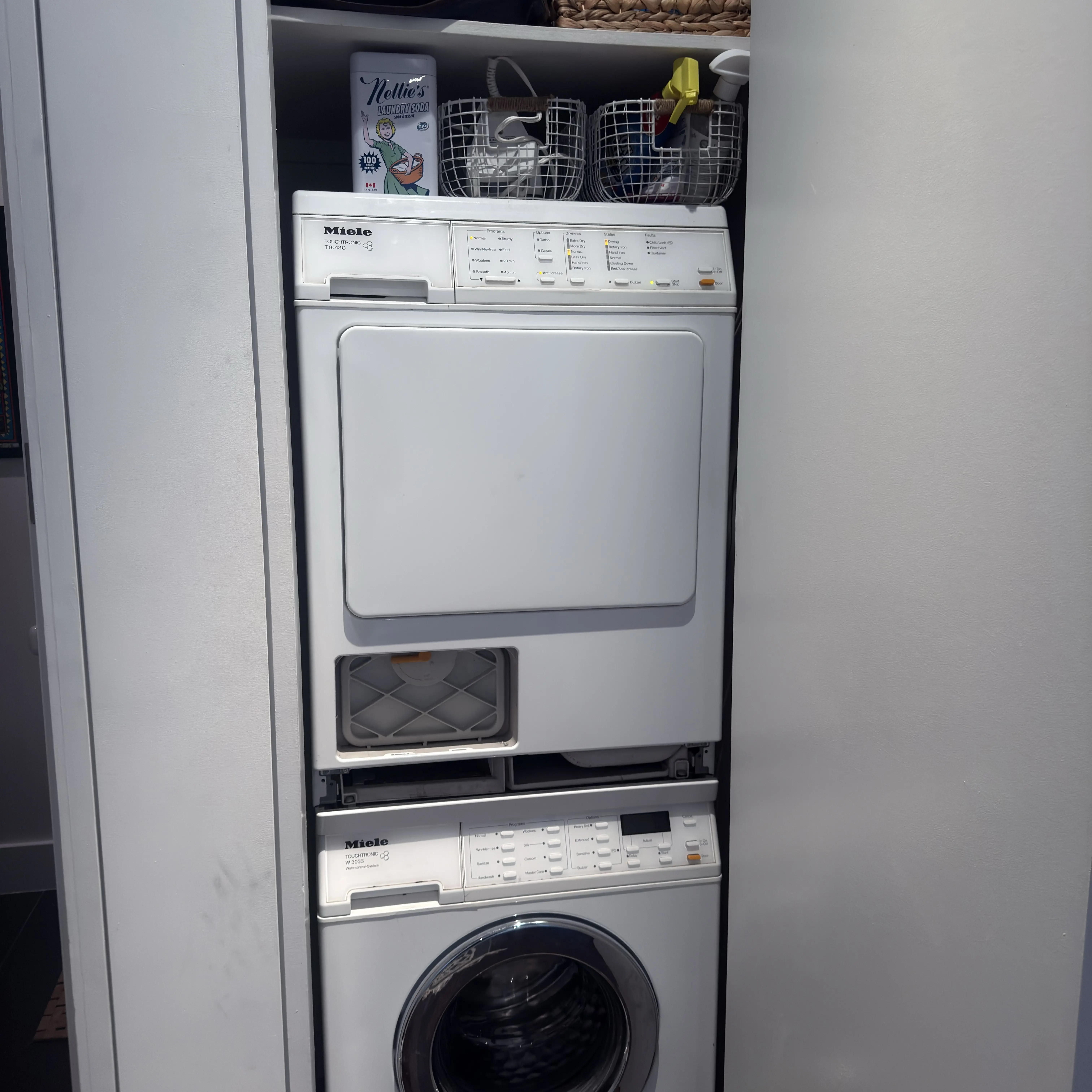 Stacked Miele washer and dryer in a white laundry closet with wire baskets