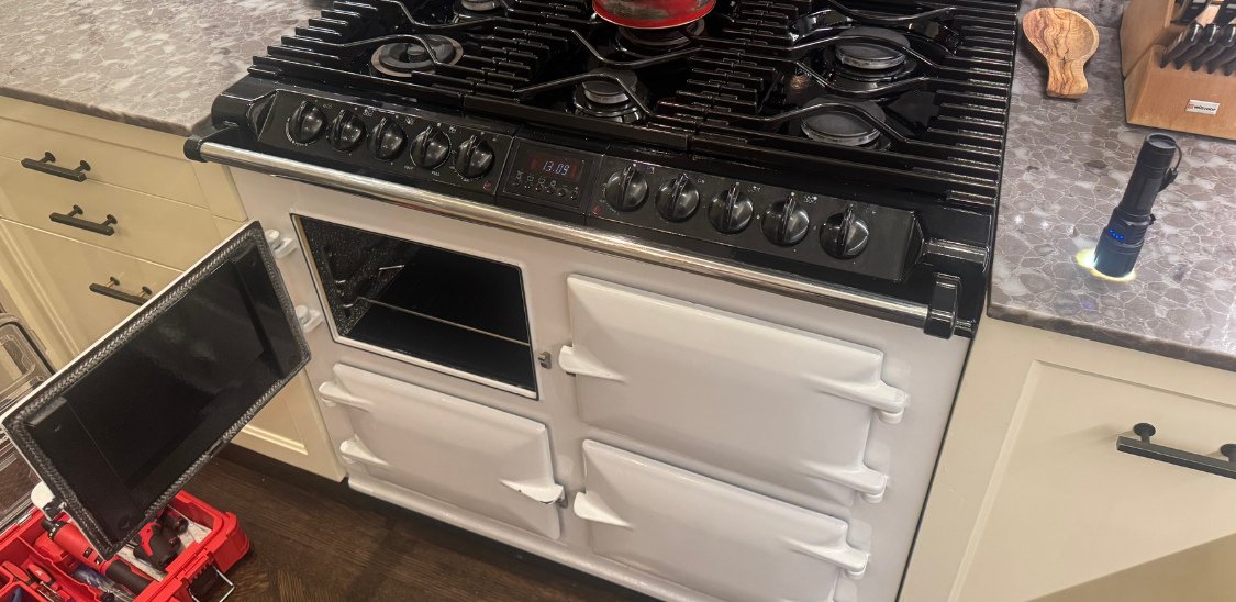 Modern kitchen corner featuring a stainless steel glass-door refrigerator, wooden cabinets, a mounted flat-screen TV, and a coffee machine on the countertop.