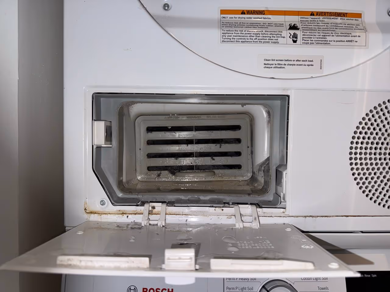 Modern kitchen corner featuring a stainless steel glass-door refrigerator, wooden cabinets, a mounted flat-screen TV, and a coffee machine on the countertop.