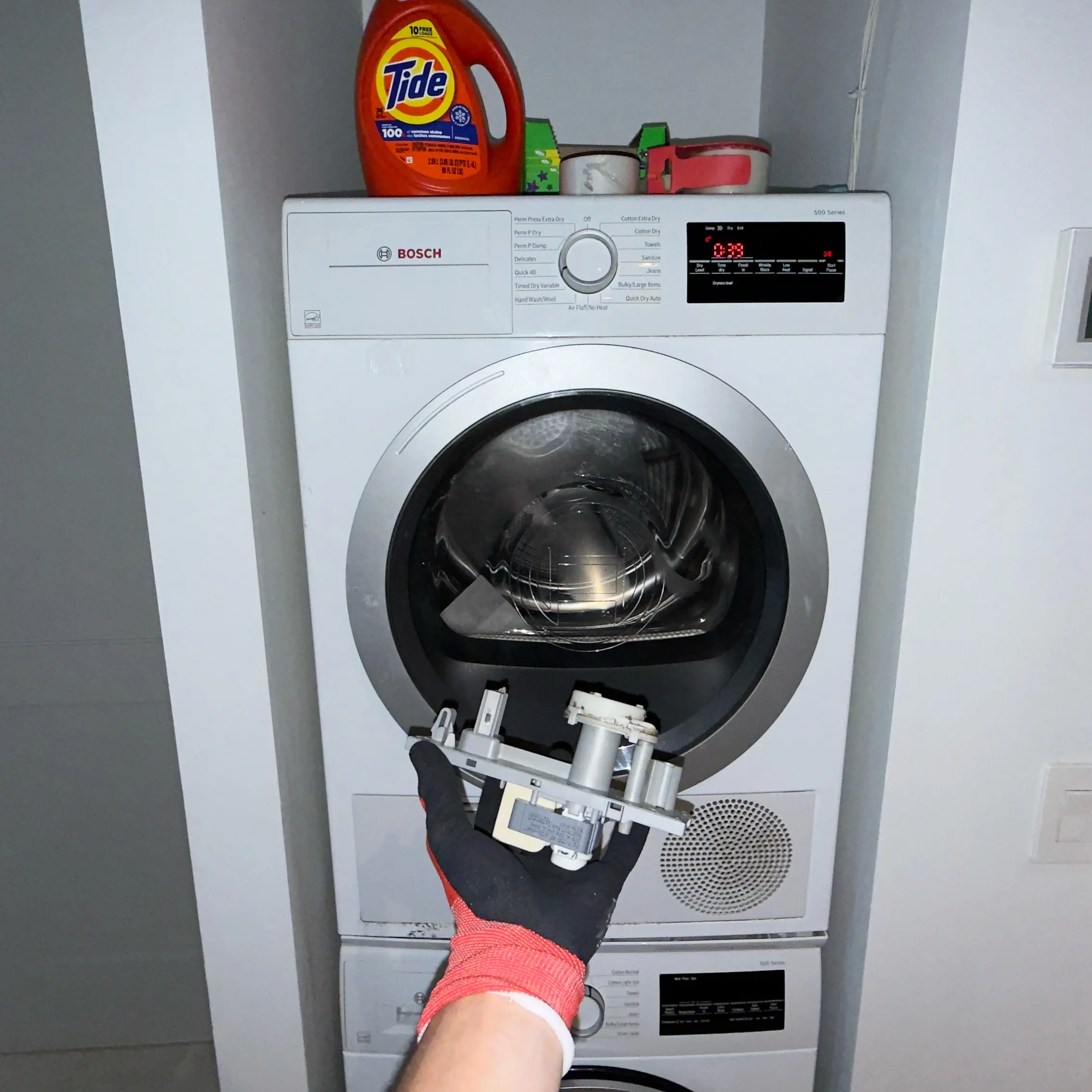 Modern kitchen corner featuring a stainless steel glass-door refrigerator, wooden cabinets, a mounted flat-screen TV, and a coffee machine on the countertop.