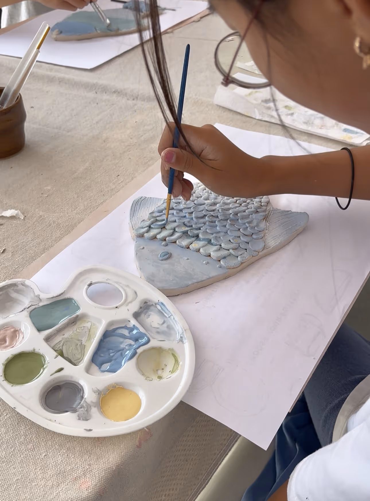 Person painting textured fish scales with a blue brush on a fish-shaped ceramic piece